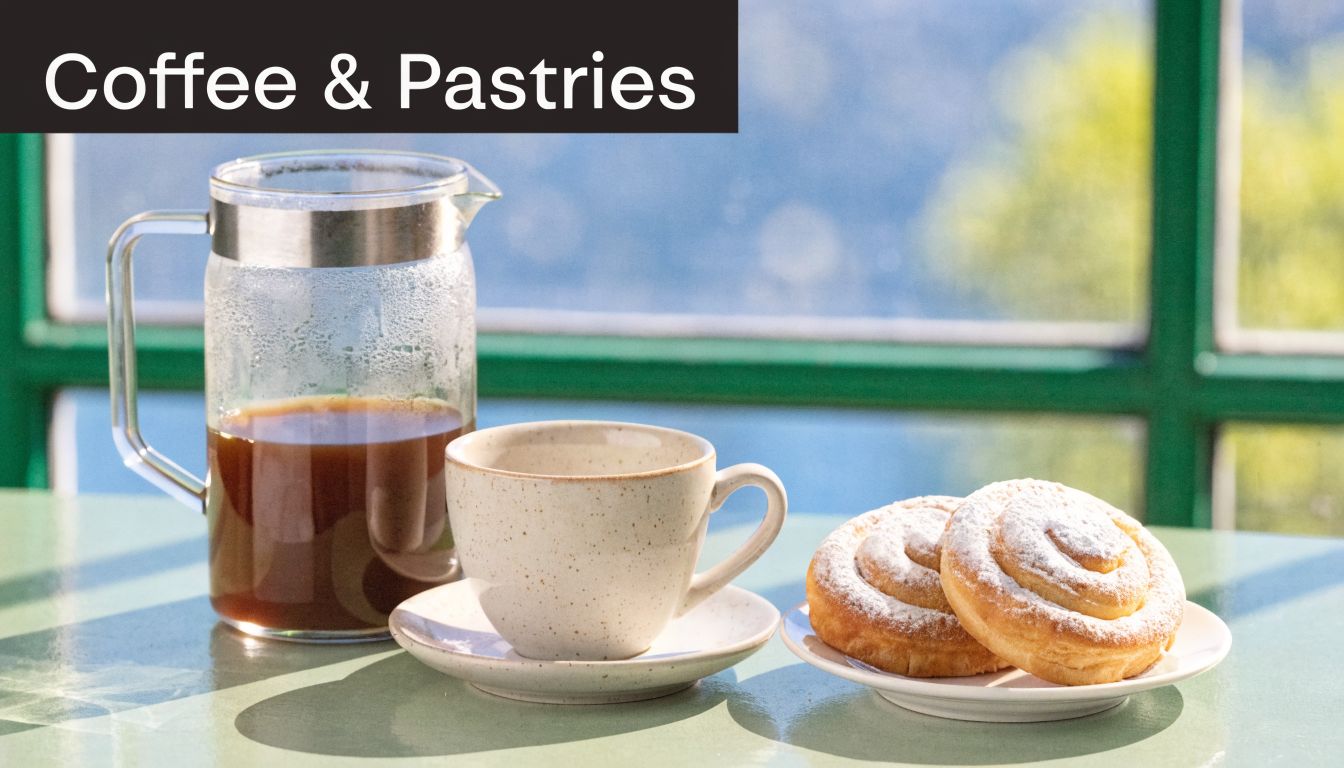 A glass coffee carafe, a ceramic cup, and two pastries covered in powdered sugar on a table.