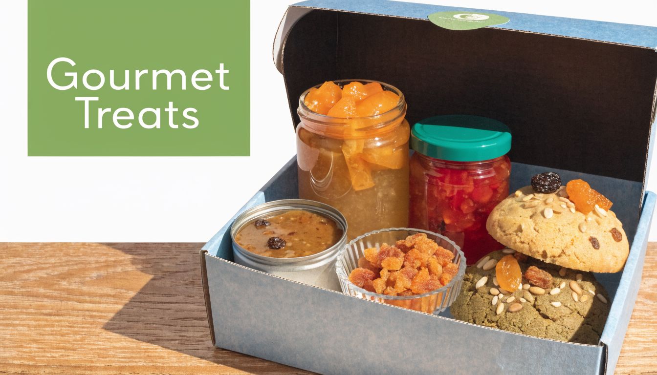 A gourmet gift box containing jars of preserves, dried fruit pieces, and two freshly baked cookies.
