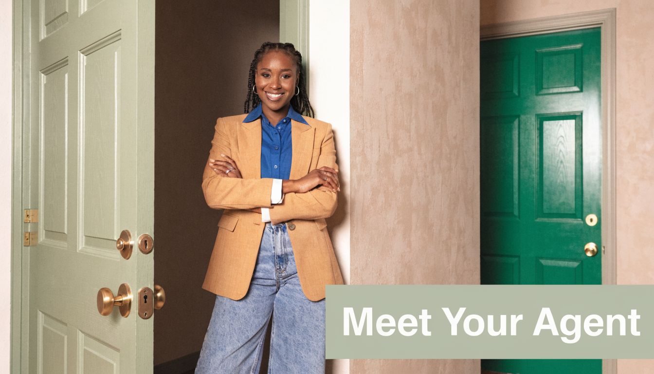 A friendly Black real estate agent standing with arms crossed in a doorway, smiling at the camera.